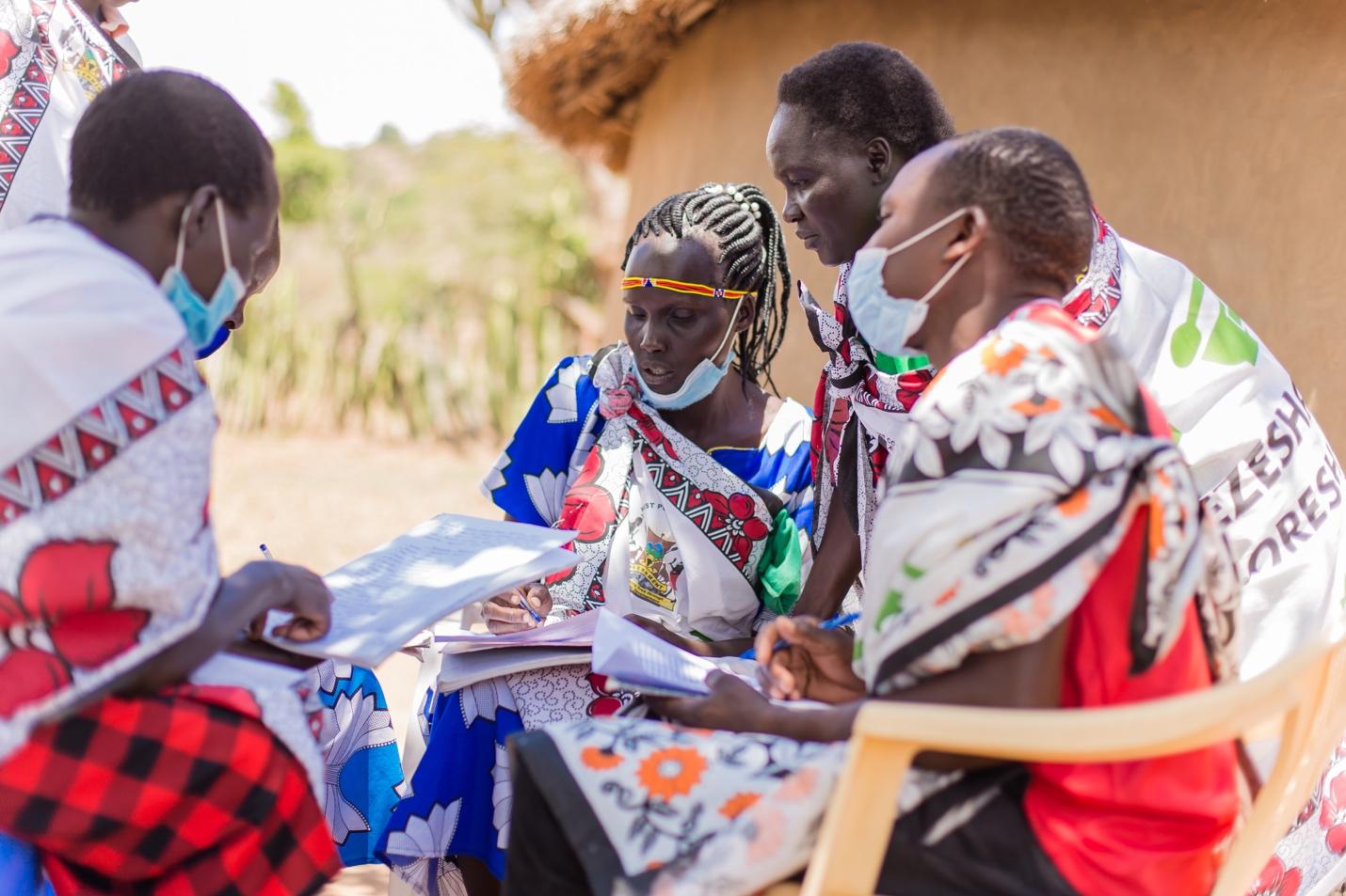 A group of women sitting outside mark attendance register 