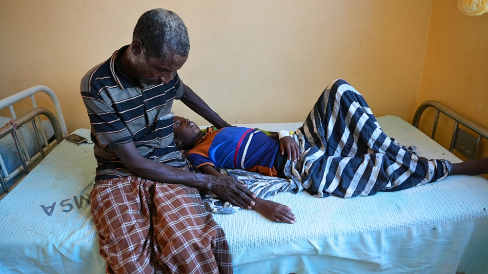 A baby lying in hospital bed held by his dad