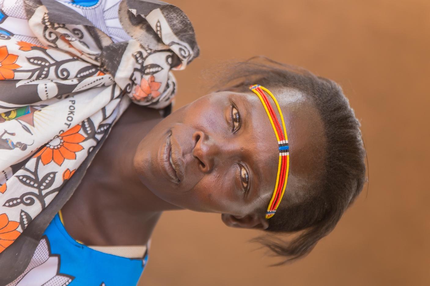 Headshot of Regina Chelimo from the shoulders up, wearing a beaded headband on her forehead and a leso tied on her right shoulder